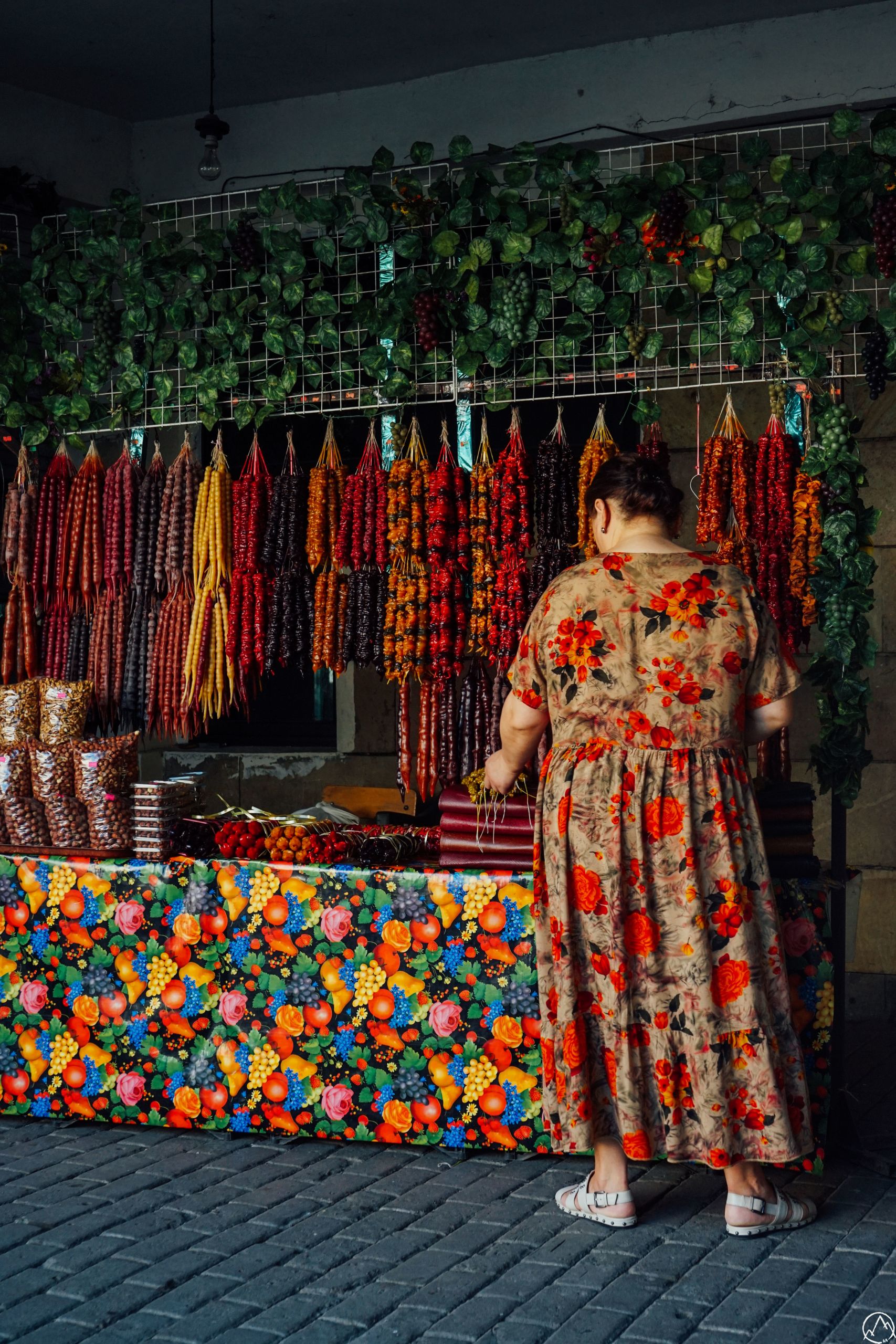 Donna in abito tradizionale georgiano circondata da tappeti colorati in un mercato locale.
